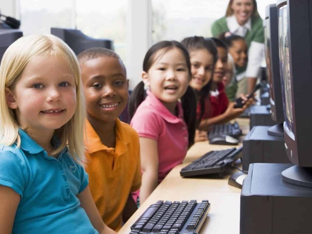 kids smiling at a row of desktop computers -examples of classroom procedures